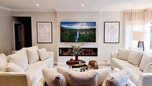 A modern living room with two sofas, a coffee table with a vase, and a large TV mounted above a fireplace. - Westbrook, Kangaroo Valley (Kangaroo Valley)