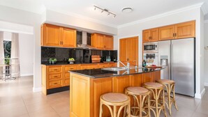 A modern kitchen with wooden cabinets, a stainless steel refrigerator, and a central island with stools. - Westbrook, Kangaroo Valley (Kangaroo Valley)