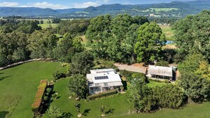 A large, open property with a house featuring a solar panel roof, surrounded by lush greenery and hills in the background. - Wild Rose Cottage Kiaroo Estate (Barrengarry, Kangaroo Valley)