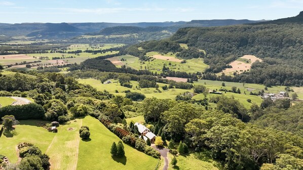 Un paisaje rural con colinas onduladas, una casa rodeada de vegetación exuberante y un cielo despejado.