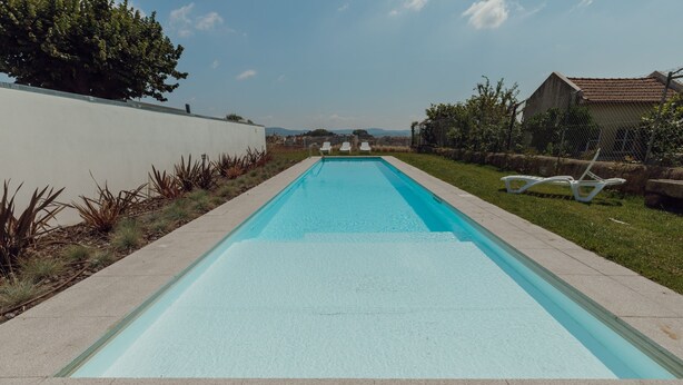 A rectangular swimming pool with a clear blue water surface, surrounded by a concrete deck and a low white wall. - Home With A Pool by Vacationy (Porto)