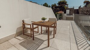 A patio with a wooden table and two chairs, a potted plant, and a white wall. - Home With A Pool by Vacationy (Porto)