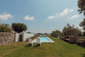 Una piscina con sillas de descanso, un muro de piedra y vistas a colinas distantes.