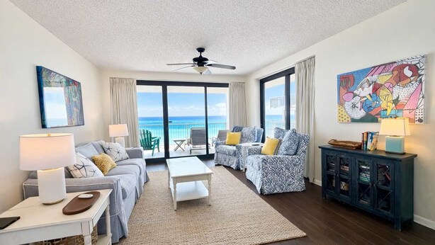 A living room with a sofa, armchair, coffee table, and a view of the ocean through large windows. - Windward Pointe 1006- Corner unit, Incredible views (Orange Beach)