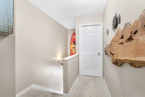 A hallway with a white door, a wooden wall art piece, and a surfboard decoration.