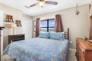 A bedroom with a bed, a ceiling fan, a dresser, a window with curtains, and a wall-mounted lamp. - Heron Landing 14- Beach access, on Little Lagoon (Gulf Shores)