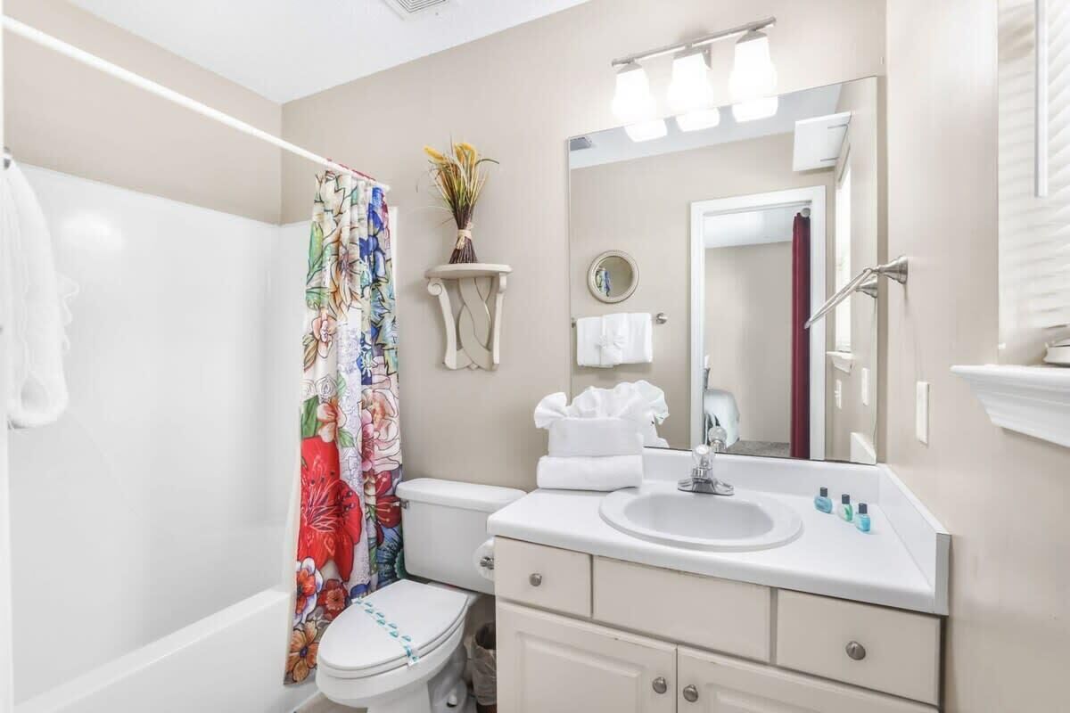 A bathroom with a toilet, sink, mirror, and shower curtain.