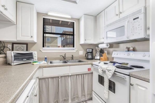 A compact kitchen with white cabinets, a built-in microwave, a stove, and a toaster. - Heron Landing 14- Beach access, on Little Lagoon (Gulf Shores)
