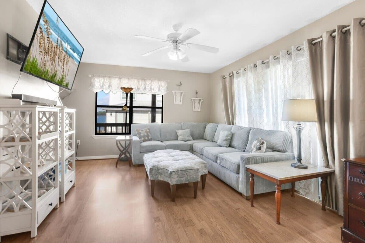 Una sala de estar con sofá, reposapiés, televisión y ventilador de techo.