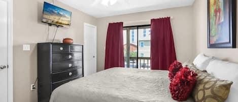 A bedroom with a bed, a dresser, a ceiling fan, a TV, and a window with curtains.