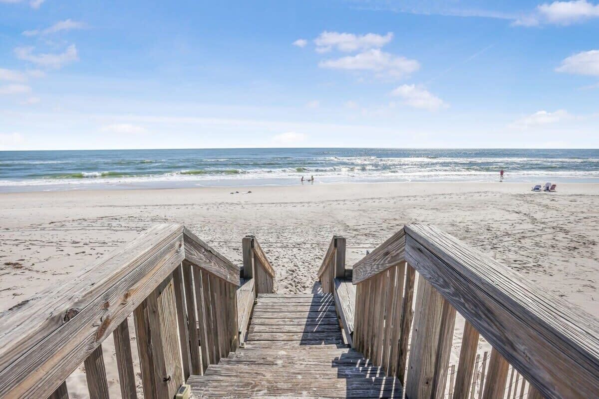 A wooden boardwalk leading to a sandy beach with the ocean in the background.