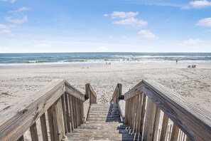A wooden boardwalk leading to a sandy beach with the ocean in the background.