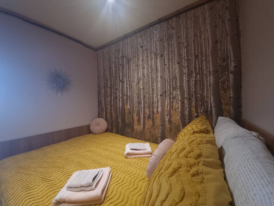Een slaapkamer met een geel bedovertrek met textuur, een wit kussen en een opgevouwen handdoek op het bed.