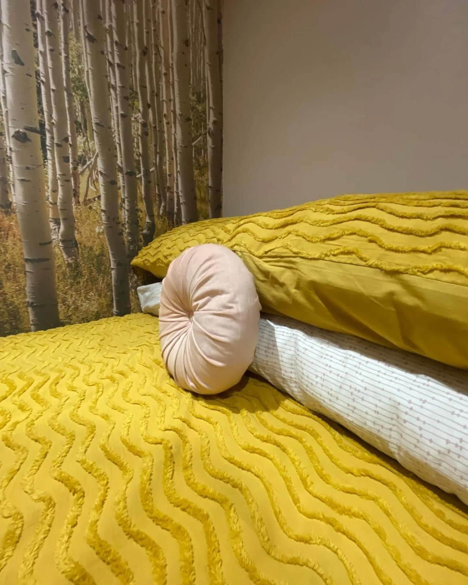 A bed with a yellow patterned bedspread and a single pillow.