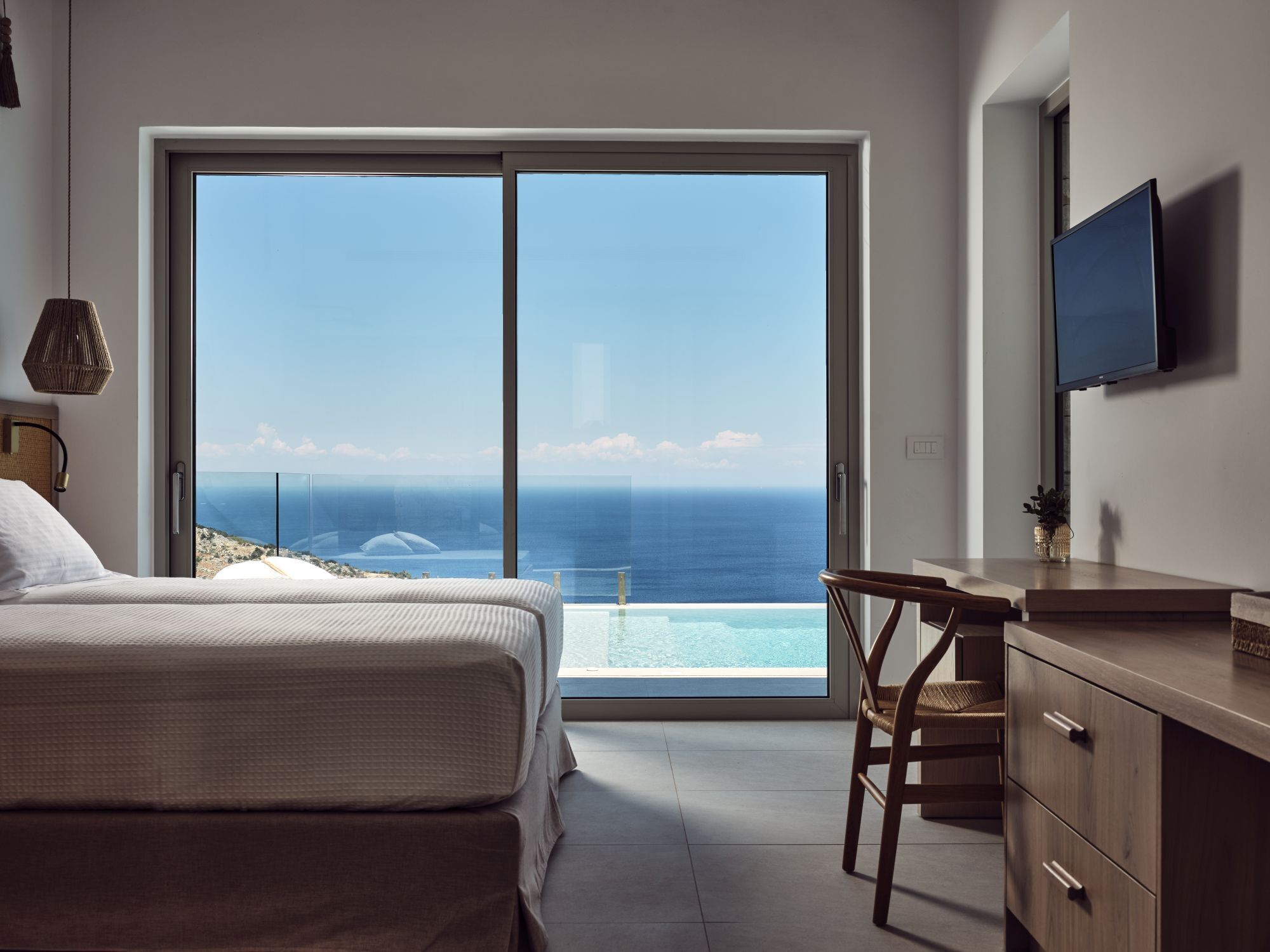 A bedroom with a large sliding glass door leading to a balcony with a view of the ocean.