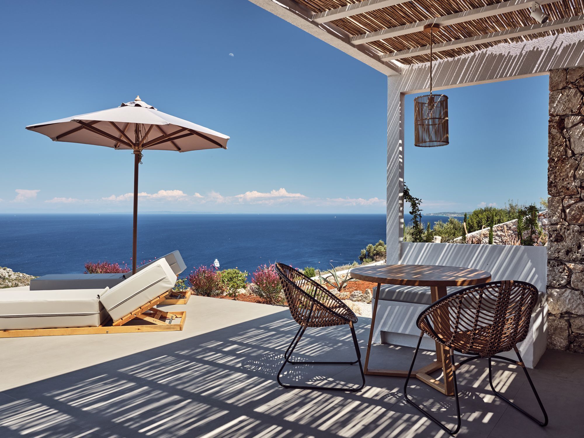 Una terraza con vistas al mar, con sillones, una mesa y una sombrilla.