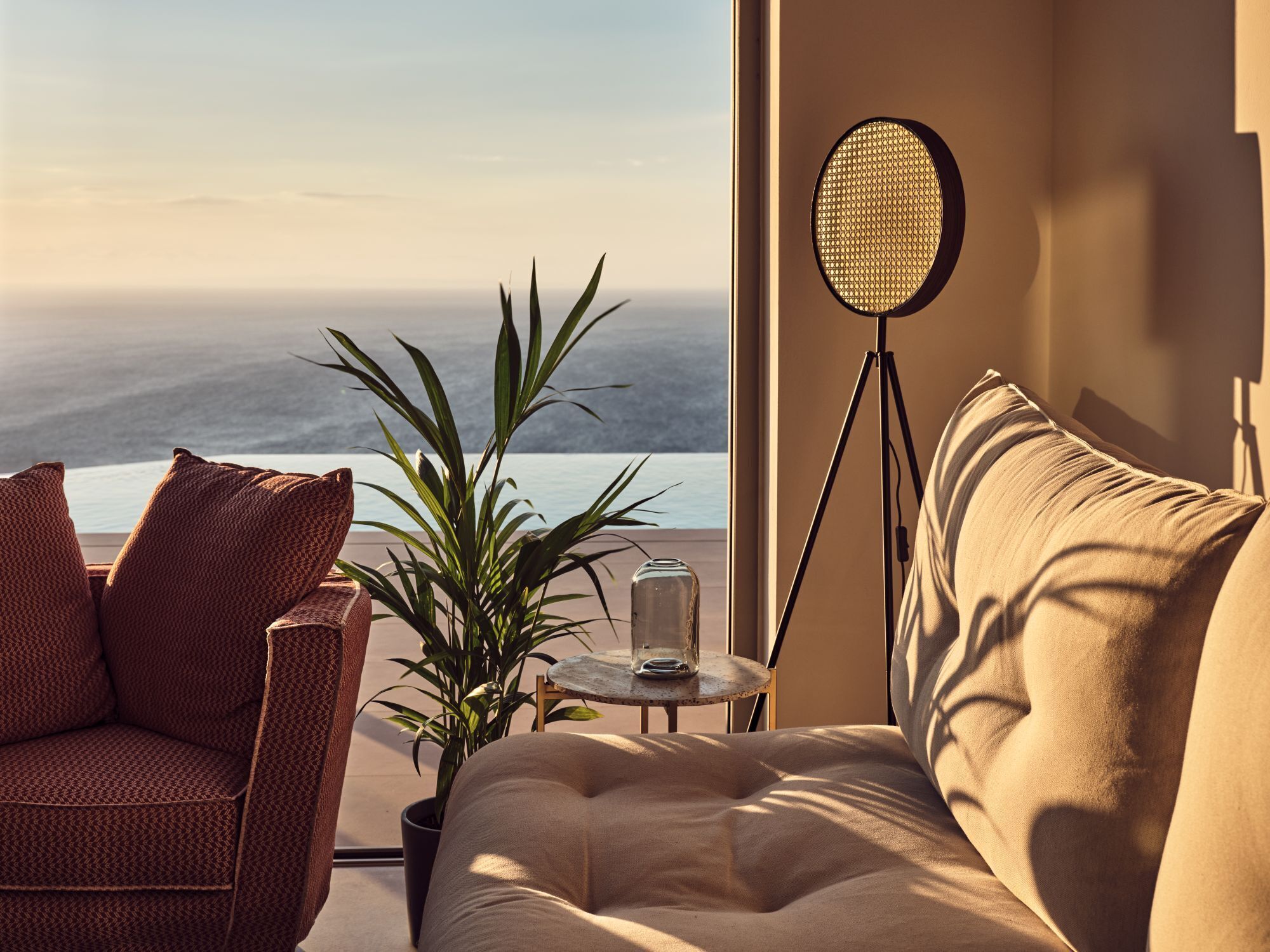 Ein gemütliches Zimmer mit Meerblick, ausgestattet mit einem Korbstuhl, einer gepolsterten Couch, einer Topfpflanze und einer Stehlampe.