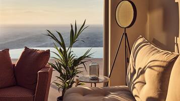 Ein gemütliches Zimmer mit Meerblick, ausgestattet mit einem Korbstuhl, einer gepolsterten Couch, einer Topfpflanze und einer Stehlampe.