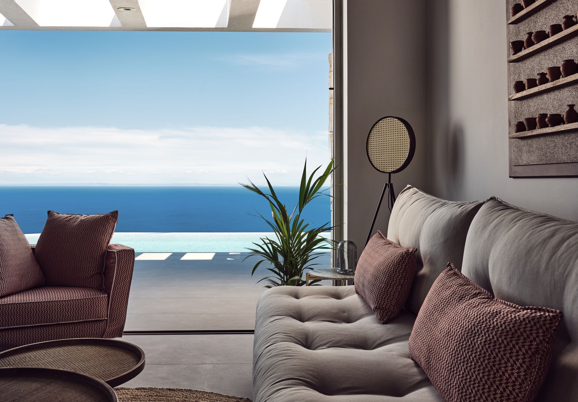A modern living room with a view of the ocean, a sofa, a chair, and a round table with a lamp.