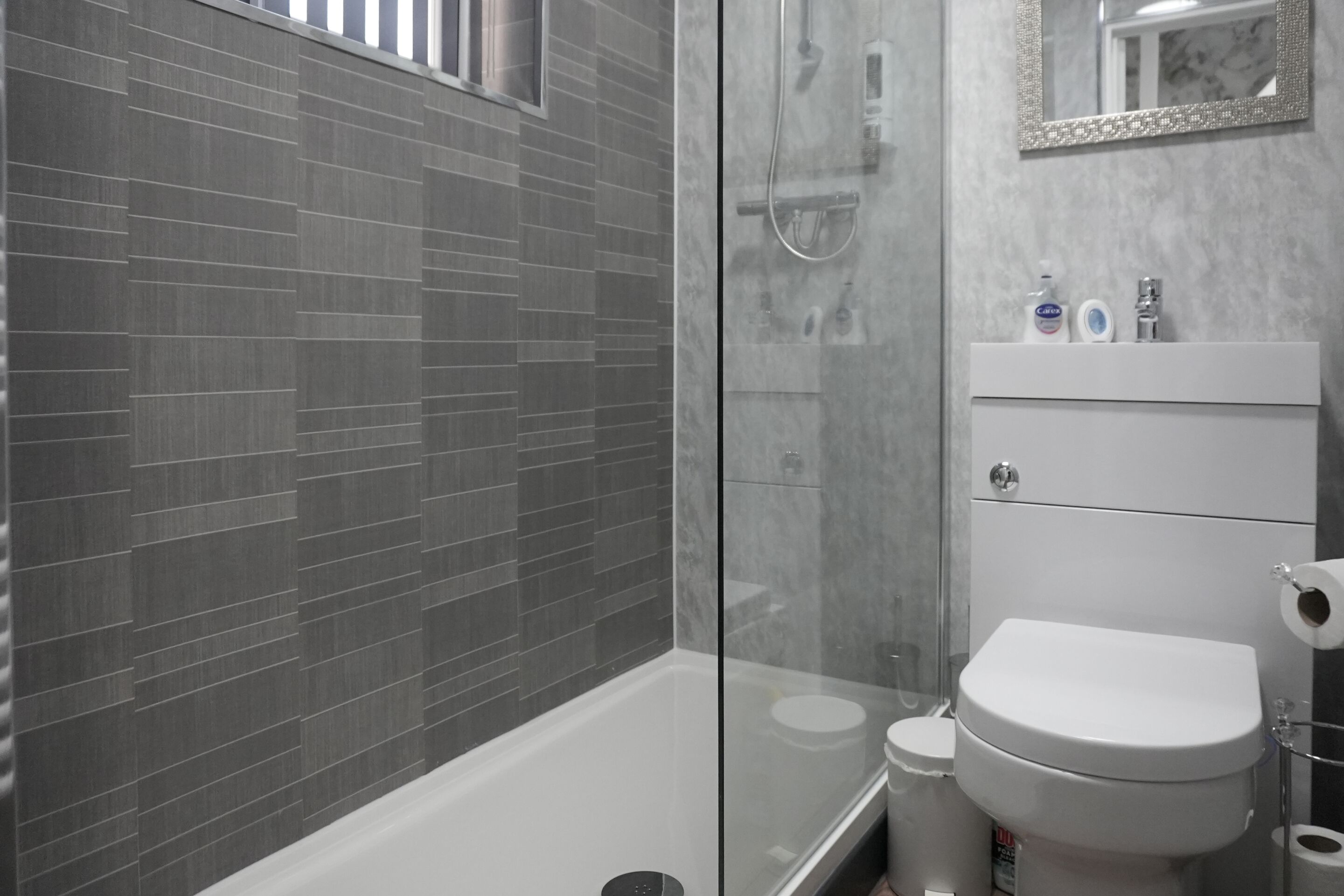 A modern bathroom with a glass shower enclosure, a white bathtub, and a white sink with toiletries.