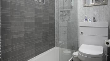 A modern bathroom with a glass shower enclosure, a white bathtub, and a white sink with toiletries.