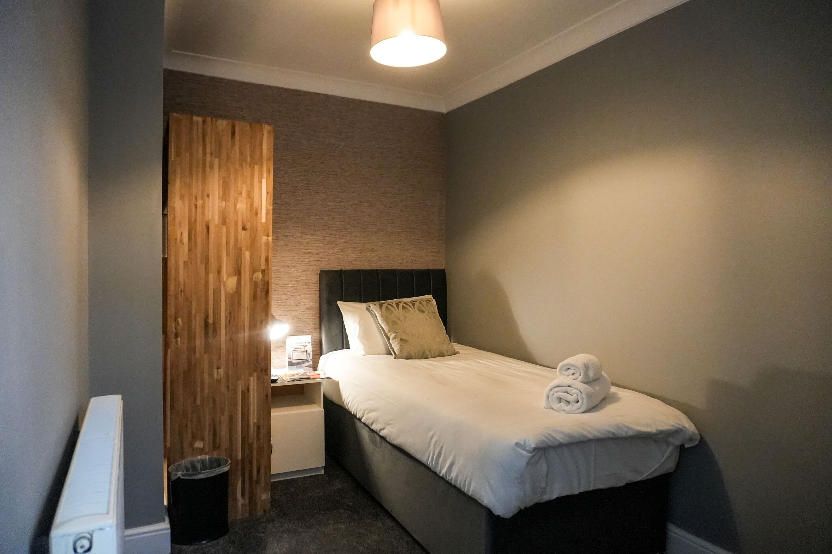 Una camera da letto piccola e ordinata con un letto singolo, un comodino, una parete divisoria in legno e un termosifone.