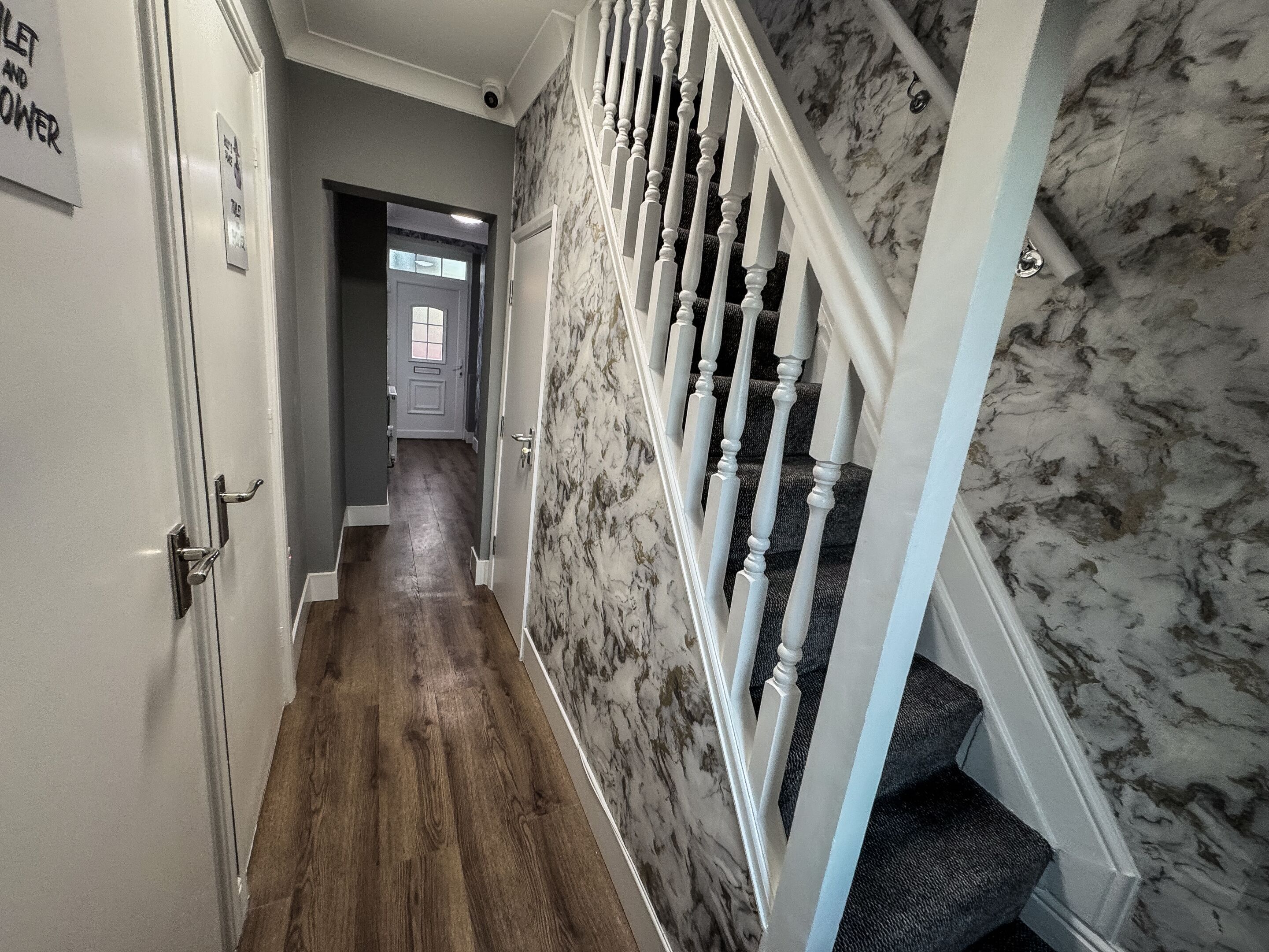 A hallway with a wooden floor, a marble wall, and a white staircase with a balustrade.