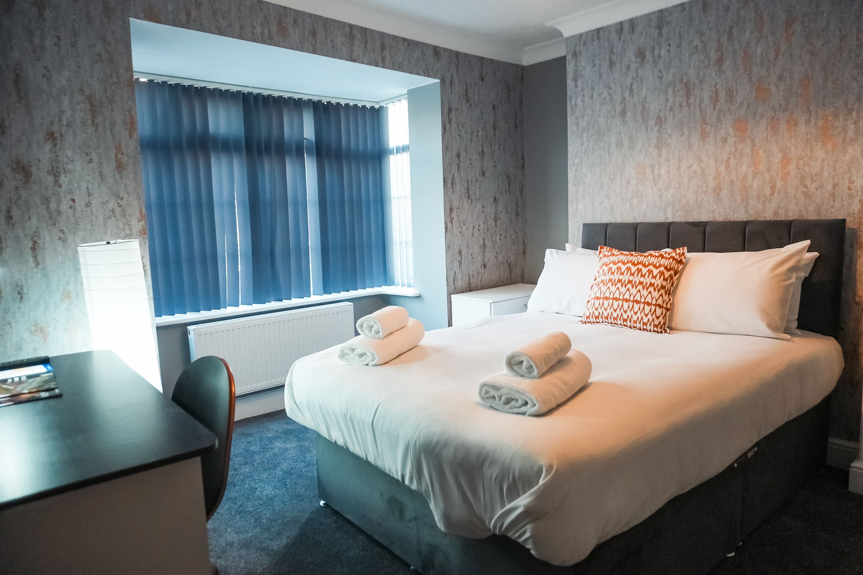 A hotel room with a bed, a desk, a chair, and a window with curtains.