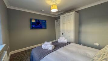 A hotel room with a bed, a television mounted on the wall, a door, and a ceiling light.