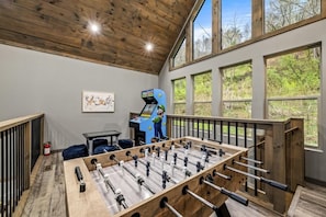 Ein Zimmer mit Kicker, Spielkonsole und großen Fenstern.