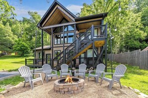 Una casa a più piani in legno con un braciere e poltrone Adirondack nel giardino.