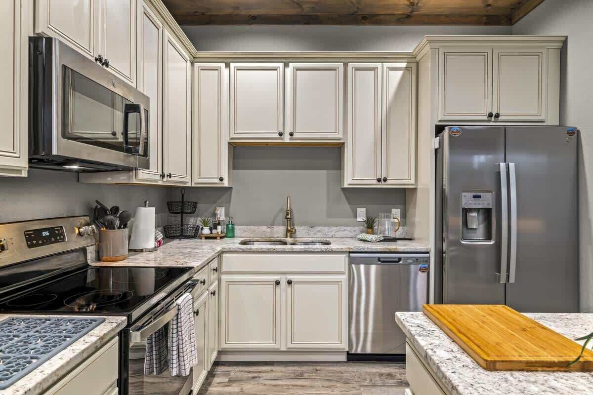 A kitchen with white cabinets, stainless steel appliances, a granite countertop, and a wooden cutting board.