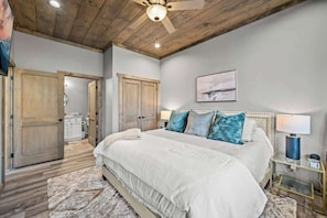 A bedroom with a large bed, wooden ceiling, and a ceiling fan.