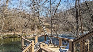 Eine Holzterrasse mit Stühlen, die auf einen Fluss mit Bäumen blickt.