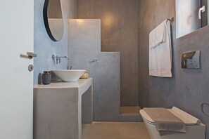 A modern bathroom with a built-in sink, a mirror, and a shower enclosure. - Vastblue (Paros)