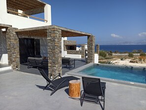 A modern outdoor pool area with stone pillars, lounge chairs, and a view of the sea. - Vastblue (Paros)