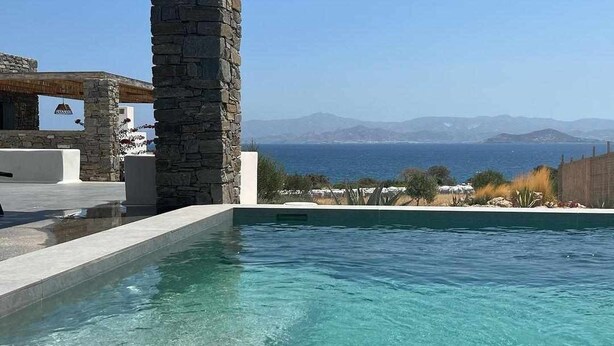 A swimming pool with clear water, stone pillars, and a view of the sea and mountains. - Vastblue (Paros)