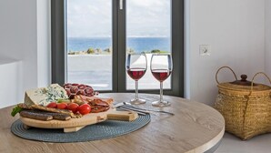 A round wooden table with a charcuterie board, two glasses of red wine, and a woven basket. - Vastblue (Paros)