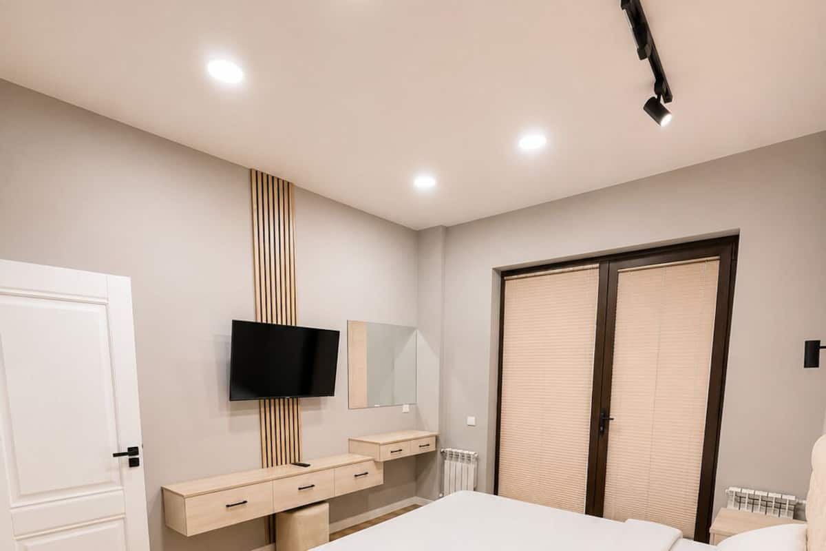 A bedroom with a bed, a TV, a dresser, a mirror, and a wardrobe.