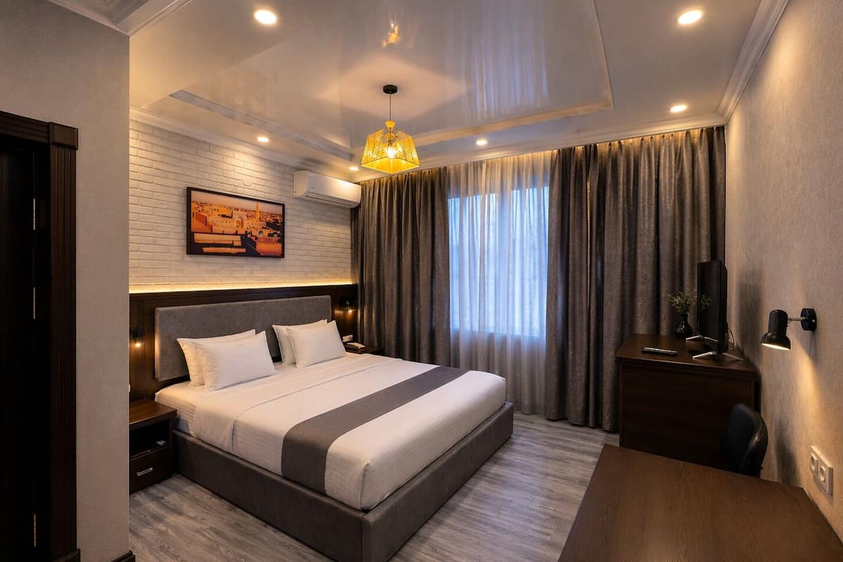 A modern hotel room with a large bed, a desk with a chair, a TV, and a painting on the wall.