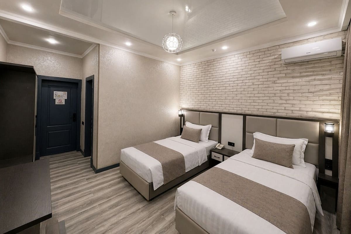 A hotel room with two beds, a brick-patterned wall, an air conditioning unit, and a desk.
