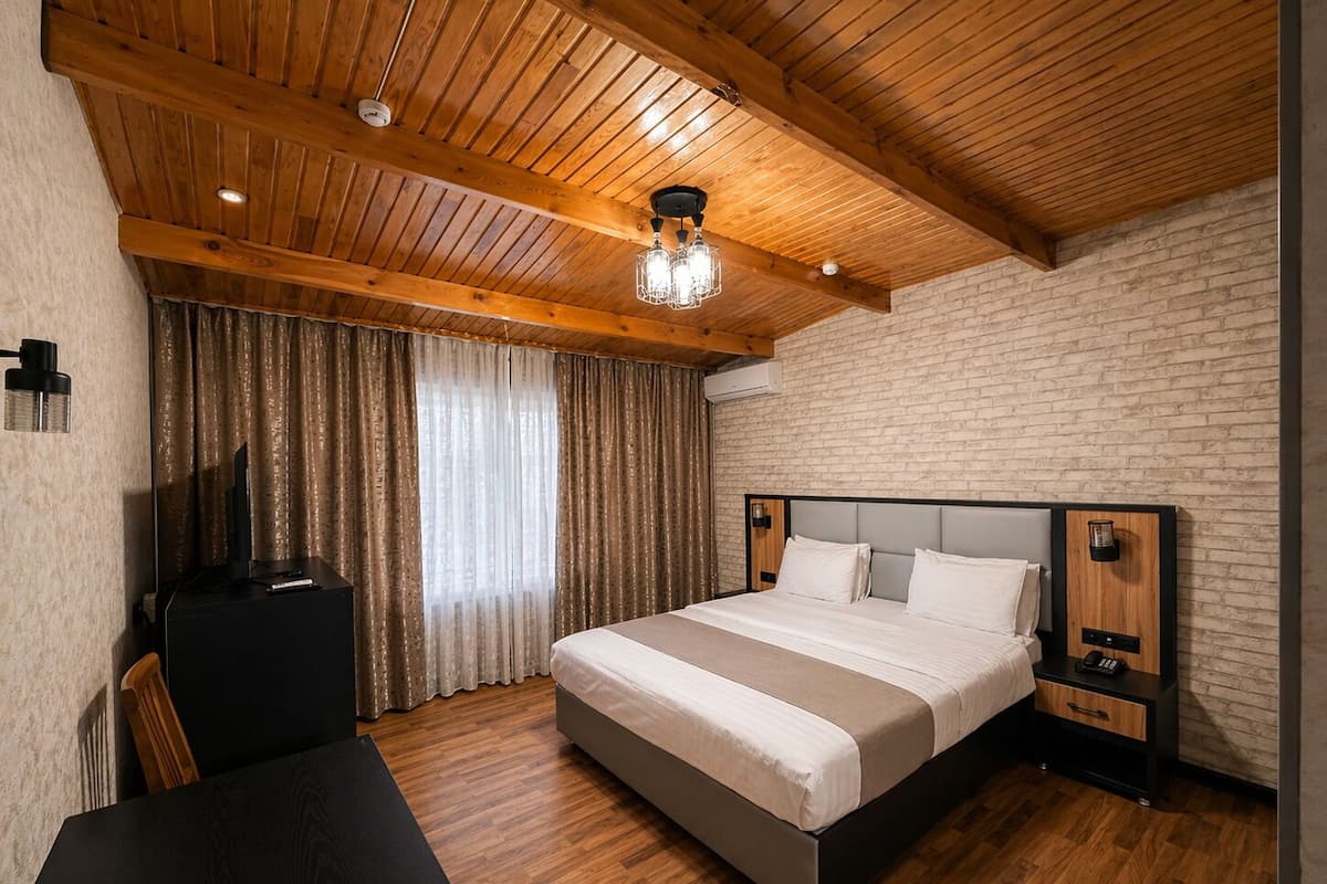 A bedroom with a bed, a desk, a chair, a TV, and a brick wall.