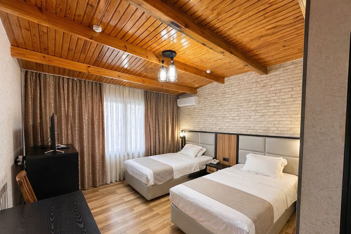 A hotel room with two beds, a desk, a TV, and a brick wall.