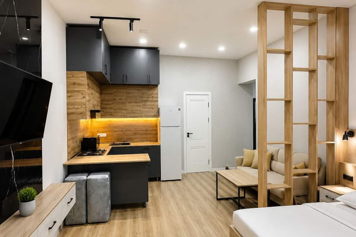 A modern bedroom with a wooden bed, a small kitchenette, and a TV on the left.