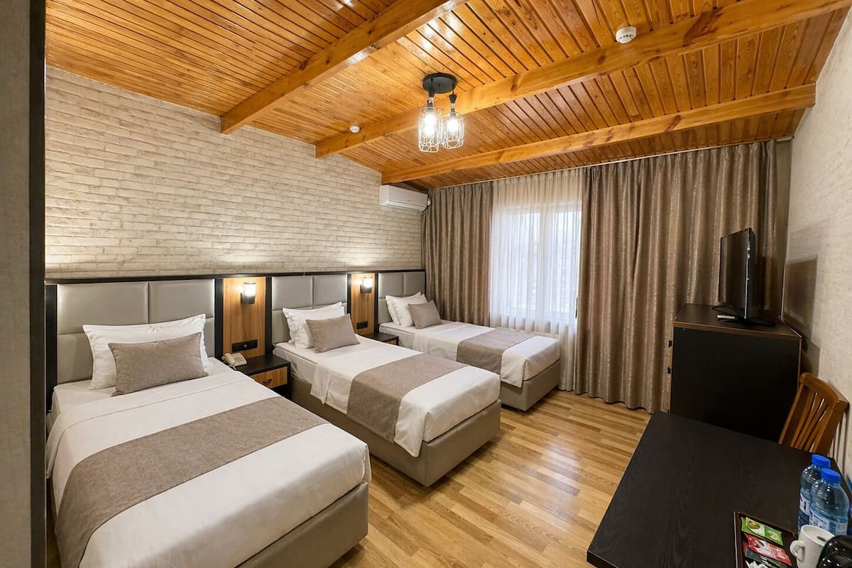 A hotel room with three beds, a television, a desk with a coffee maker, and a brick wall.