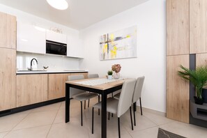 A modern kitchen with white cabinets, a black microwave, and a dining table with chairs. - Superiour App 25m From the Sea! City Umag-croatia!! Top Property!! Garden Palace (Umag)