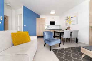 A modern living room with a sofa, a blue chair, and a dining area with a table and chairs. - Superiour App 25m From the Sea! City Umag-croatia!! Top Property!! Garden Palace (Umag)
