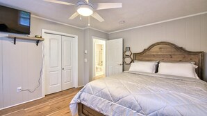 Un dormitorio con cama, ventilador de techo, televisor montado en la pared y una puerta que da a otra habitación.