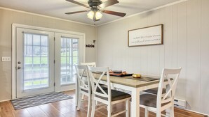 Un comedor con una mesa dispuesta para cuatro, sillas blancas, un ventilador de techo y una cita enmarcada en la pared.