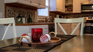 Una cocina con armarios blancos, un microondas y una mesa de madera con una bandeja que sostiene una vela roja, un adorno blanco y un adorno a rayas.